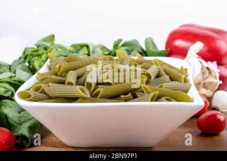 Glutenfreie Penne Pasta aus grünen Erbsen auf Holzbrett. basilikum, Tomaten und Knoblauch. Schuss von oben und closeup.Food Hintergrund italienische Penne Stockfoto