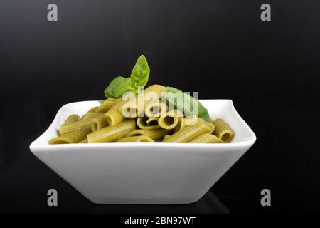 Glutenfreie, frisch gekochte Penne-Pasta aus grünen Erbsen auf schwarzem Hintergrund isoliert. basilikum auf der Oberseite, in einer weißen Schüssel. Von oben geschossen und Nahaufnahme.Food Bac Stockfoto