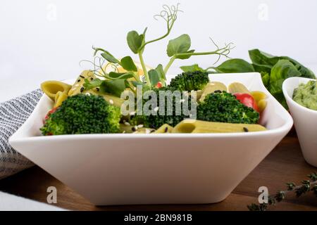 Glutenfreie, frisch gekochte Penne-Pasta aus grünen Erbsen auf Holzbrett isoliert. basilikum, Tomaten, Avocado und Koriander in einer weißen Schüssel. Schuss von oben Stockfoto