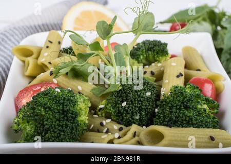 Glutenfreie, frisch gekochte Penne-Pasta aus grünen Erbsen auf Holzbrett isoliert. basilikum, Tomaten, Avocado und Koriander in einer weißen Schüssel. Schuss von oben Stockfoto
