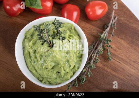 Glutenfreie, frisch gekochte Penne-Pasta aus grünen Erbsen auf Holzbrett isoliert. basilikum, Tomaten, Avocado und Koriander in einer weißen Schüssel. Schuss von oben Stockfoto