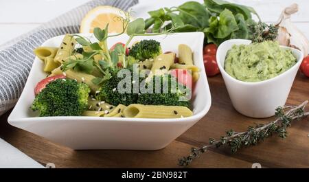 Glutenfreie, frisch gekochte Penne-Pasta aus grünen Erbsen auf Holzbrett isoliert. basilikum, Tomaten, Avocado und Koriander in einer weißen Schüssel. Schuss von oben Stockfoto