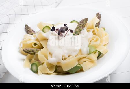 Frische hausgemachte Pasta Gericht Fettuccine oder Tagliatelle, grüner Spargel, weiße Sauce, in einem weißen Teller auf Holz weißen Hintergrund Tisch Stockfoto