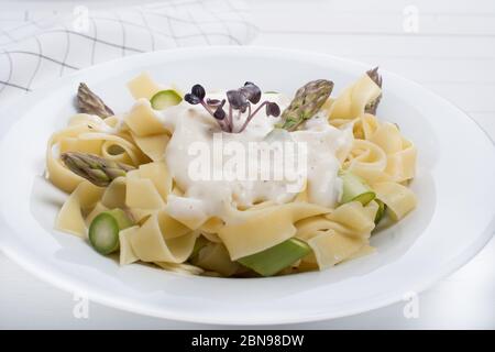 Frische hausgemachte Pasta Gericht Fettuccine oder Tagliatelle, grüner Spargel, weiße Sauce, in einem weißen Teller auf Holz weißen Hintergrund Tisch Stockfoto