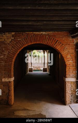 Blick vom Gebäude auf einen kleinen schmalen Kanal zwischen den Häusern in Venedig, Italien. Ein Blick aus einem Tunnel mit Backsteinwänden, zwei antiken Säulen und Stockfoto