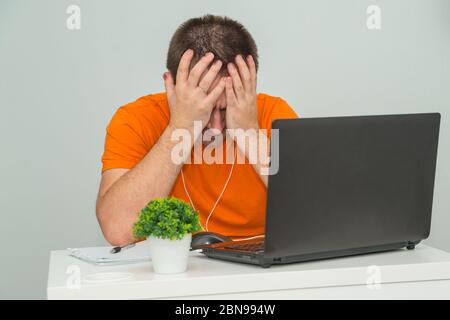 Müde überarbeiteter Mann hält seinen Kopf in der Nähe des Laptops sitzen. Online-Arbeit. Online-Bildungskonzept Stockfoto