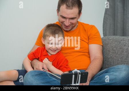 Junge und Mann, die während eines Online-Anrufs auf das Smartphone schauen und lächeln. Bleiben Sie zu Hause und Fernkommunikation Konzept Stockfoto