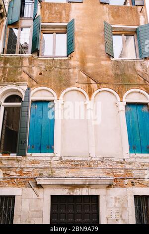 Nahaufnahmen von Fassaden in Venedig, Italien. Die Fassade eines fünfstöckigen Gebäudes mit klassischen venezianischen Bogenfenstern mit Holzfenstern. Der Stockfoto