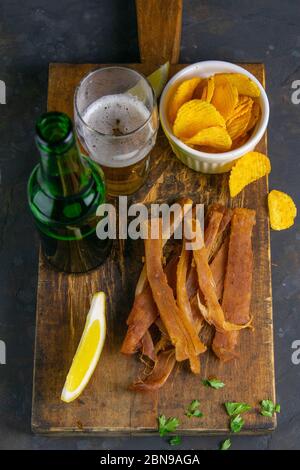 Peruanischer Tintenfisch mit Bier, Zitrone und Kartoffelchips auf dunklem Holzbrett. Snack auf Fisch mit Bier. Nahaufnahme Stockfoto