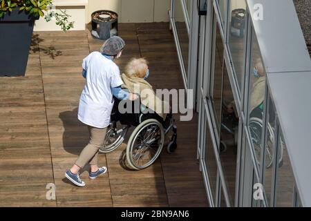 Krankenschwester Pflege einer älteren und behinderten Frau in einem Pflegeheim an einem sonnigen Tag während der Coronavirus-Pandemie Covid-19. Beide tragen eine Gesichtsmaske. Stockfoto