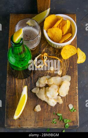 Getrockneter Oktopus mit Bier, Zitrone und Kartoffelchips auf dunklem Holzbrett. Snack auf Fisch mit Bier. Nahaufnahme Stockfoto