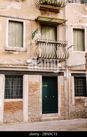 Nahaufnahmen von Fassaden in Venedig, Italien. Grüne Holztür am unteren Rand des Backsteinhauses. Balkon mit geschmiedetem Zaun. Eine alte Straßenlampe auf der Stockfoto