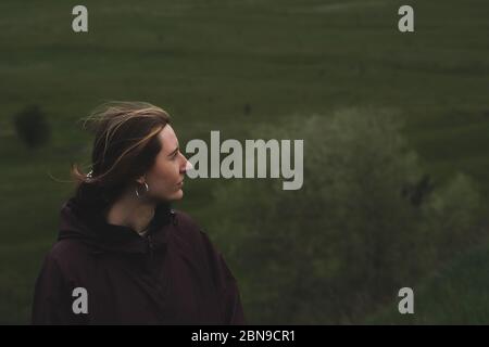 Frau in einem Regen Anorak steht auf dem Hügel, tiefgrünem Hintergrund. Wandern, Wandern und verbringen Freizeit im Freien, junge Erwachsene Portait Stockfoto