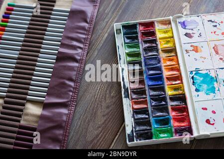 Farbstifte, Pinsel und Aquarellfarben auf Holztisch. Kunstmaler Accessoires Stockfoto