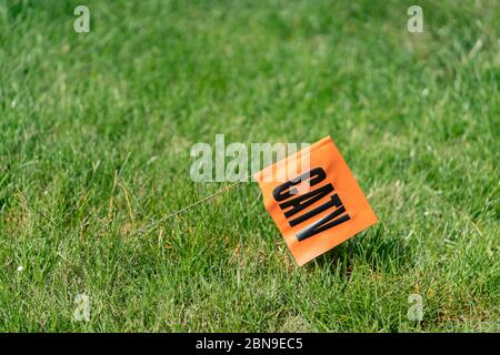 CATV in schwarzen Buchstaben auf einer orangefarbenen Flagge in einem grünen Rasen für Anruf stecken, bevor Sie Service graben Stockfoto