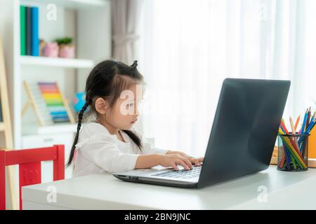 Asiatische Kindergarten Schule Mädchen Videokonferenz E-Learning mit Lehrer auf Laptop im Wohnzimmer zu Hause. Homeschooling und Fernstudium, online Stockfoto