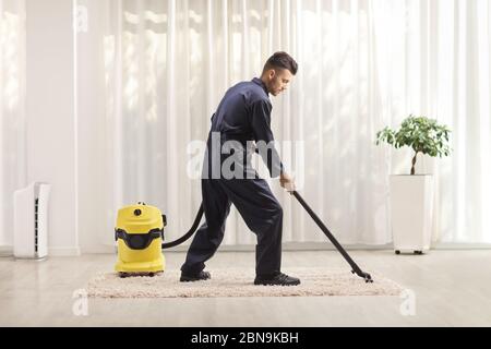 In voller Länge Aufnahme eines Mannes in einer Uniform, der einen Teppich in einem Haus saugt Stockfoto
