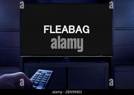 Ein Mann zeigt eine Fernbedienung auf den Fernseher, der den Hauptbildschirm des Fleabag anzeigt (nur redaktionelle Verwendung). Stockfoto
