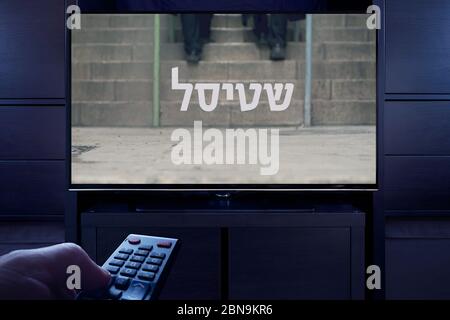 Ein Mann zeigt eine Fernbedienung auf den Fernseher, der den Shtisel-Hauptbildschirm anzeigt (nur redaktionelle Verwendung). Stockfoto