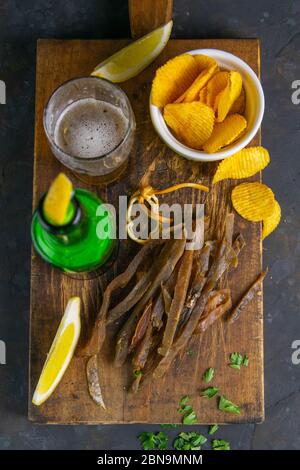 Getrocknete Karpfen-Fischstäbchen mit Bier, Zitrone und Kartoffelchips auf dunklem Holzbrett. Snack auf Fisch mit Bier. Nahaufnahme Stockfoto