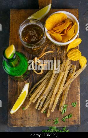 Getrockneter gesalzener Thunfisch-Elite-Snack mit Bier, Zitrone und Kartoffelchips auf dunklem Holzbrett. Snack auf Fisch mit Bier. Draufsicht, Nahaufnahme Stockfoto