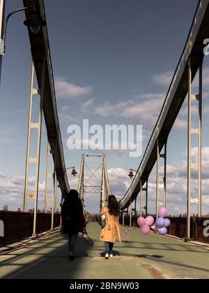 Junge Frauen mit Luftballons in den Händen gehen über Brücke Stockfoto