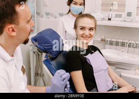 Ein schönes Mädchen sitzt auf dem Zahnarztstuhl und hört dem Arzt und seinem Assistenten zu. Zahnarzt Termin und zahnärztliche Versorgung. Stockfoto