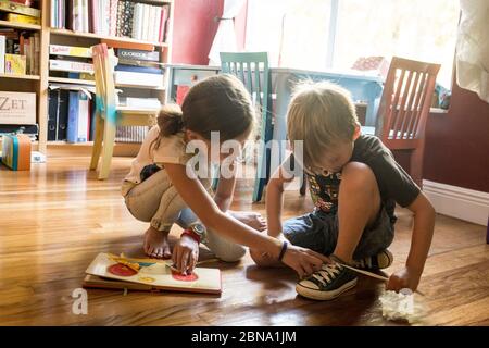 Ein junges Mädchen hilft ihrem kleinen Bruder, als er versucht, seine Schnürsenkel zu binden Stockfoto