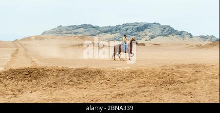 Ein älterer peruanischer Mann, der ein Stufenpferd in der nördlichen Sandwüste Perus bei Trujillo reitet. Stockfoto