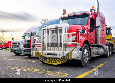 Bright Red leistungsstarke große Rig Sattelschlepper mit Übergröße Last Zeichen auf dem Grill Schutzbügel stehen mit geladenen Sattelauflieger in Reihe auf dem LKW-Stopp wi Stockfoto