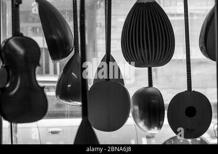 Graustufenaufnahme verschiedener Musikinstrumente, die von der Decke hängen Im Laden Stockfoto