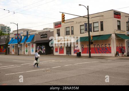 Vancouver, Kanada, 4. Mai 2020. Eine junge Frau, die Einkaufstaschen trägt, überquert die South Granville Street während der COVD-19 Pandemie.im Hintergrund sind Geschäfte mit bunten Wandmalereien bemalt. Stockfoto