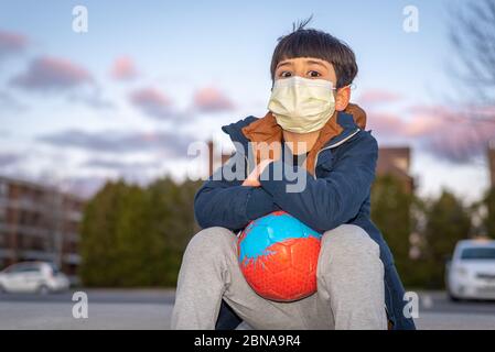 Kind spielt mit Fußball trägt Maske im Hinterhof während Roman Coronavirus Covid-19 Ausbruch und Quarantäne Stockfoto