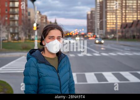 Covid-19 Pandemie Coronavirus Konzept. Junge schöne Frau in schützenden medizinischen Gesichtsmaske auf der Straße an der Straße stehend. Stockfoto