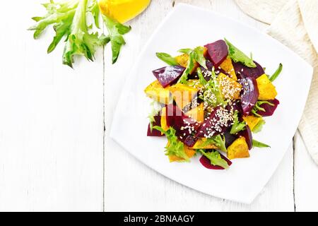 Salat aus gebackenem Kürbis, gekochten Rüben, Rucola, gewürzt mit Essig, Gewürzen, Orangensaft und Pflanzenöl in einem Teller, Serviette auf Holzbrett backgr Stockfoto