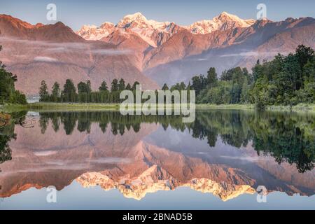 Schneebedeckte Berggipfel des Mount Cook und Mount Tasman spiegeln sich im Lake Matheson im Abendlicht, Westland National Park, Fox Glacier, Whataroa, We Stockfoto