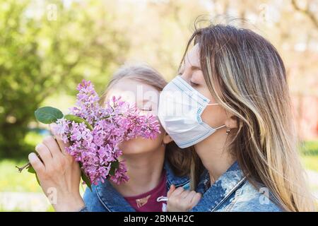 Mutter und Tochter schnüffeln auf der Straße einen Flieder. Quarantäne beenden Konzept Stockfoto