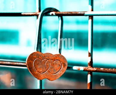 Schloss aus rostigen Herzen auf einem Gitter befestigt. Blaugrün und orange Filter. Konzept der Liebe beenden Stockfoto
