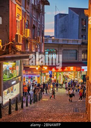 Menschen, die auf der Rua de S. Paulo (Dasanba) Straße in der Dämmerung beleuchtet. Macau, China. Stockfoto