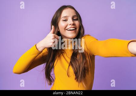 Bild von jungen schönen Frau mit langen braunen Haaren gesturing und unter Selfie-Foto-Cellhone isoliert über violettem Hintergrund Stockfoto