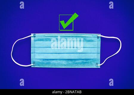 COVID-19 Prävention durch Tragen einer Maske Empfehlung mit grünem Häkchen als gute Wahl, um einen Gesichtsschutz als vorbeugende Maßnahme gegen Coronavirus zu tragen. Draufsicht der chirurgischen Ohrbügel-Masken. Stockfoto