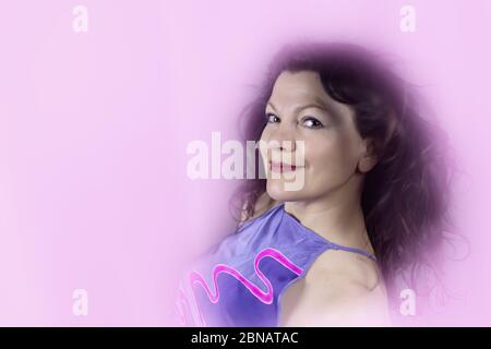 Porträt einer schönen modischen Frau mittleren Alters mit langen dunklen Haaren, das Bild ist rosa getönt. Das Konzept der Erhaltung der Jugend in jedem Alter. Stockfoto