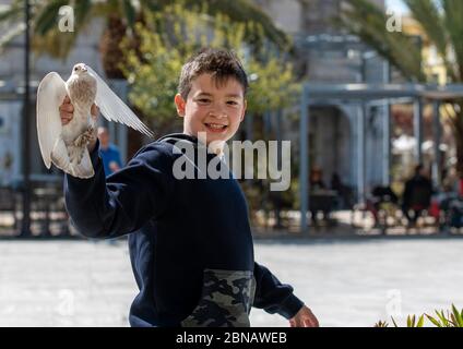 Süß und voller Freude Junge, spielt auf dem Platz, während der Fütterung der Tauben er schließlich geschafft, eine zu fangen. Begeisterung ist in seinem Gesicht zu sehen. Stockfoto