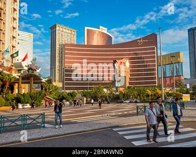 Fußgänger überqueren die Avenida do Infante Dom Henrique Straße mit dem Wynn Macau, ein Luxushotel und Casino, im Hintergrund. Macau, China. Stockfoto