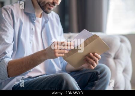 Männliche Hände ziehen einen Brief aus einem Papierumschlag. Stockfoto