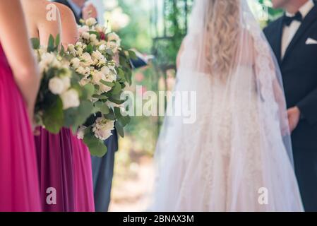 Brautjungfern in rosa Kleidern mit weißen Blumensträußen mit der Braut Und der Bräutigam dahinter Stockfoto