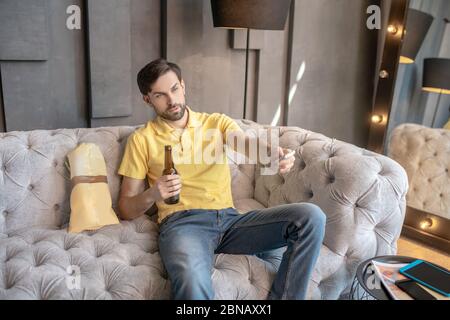 Erwachsener junger Mann mit Bier und Chips zu Hause auf dem Sofa. Stockfoto