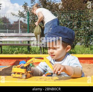 POSEN, POLEN - 14. Mai 2016: Unidentifizierter, zweijähriger Junge, der an einem sonnigen Tag mit einem Plastikspielzeugbagger an einer Sandkiste auf einem Spielplatz spielt. Stockfoto