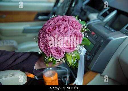 Frau mit Verlobungsblumen, rosa Rosen im Auto. Der Bräutigam hielt einen Strauß rosa Blumen im Auto. Stockfoto