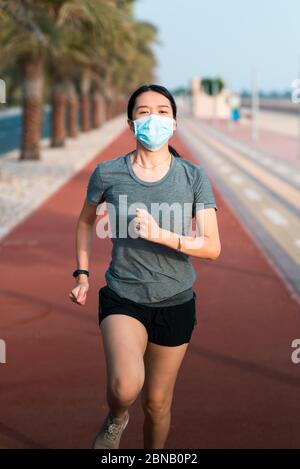 Asiatische Frau joggen auf der Laufstrecke tragen schützende chirurgische Maske, um die Ausbreitung des Coronavirus zu verhindern und sicher zu bleiben Stockfoto